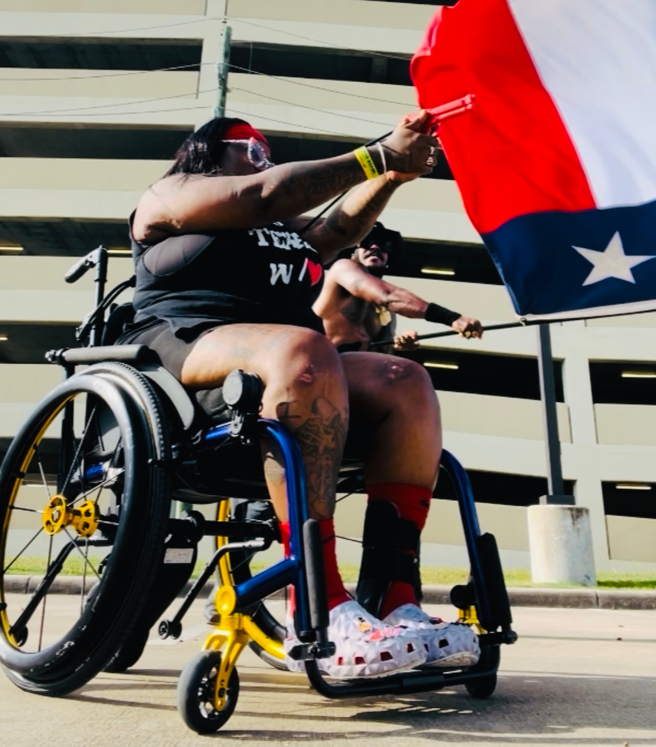 Woman of color in wheelchair training with GRUPS® Grip Trainer, Texas flag waiving during outdoor empowerment session, self defense training.